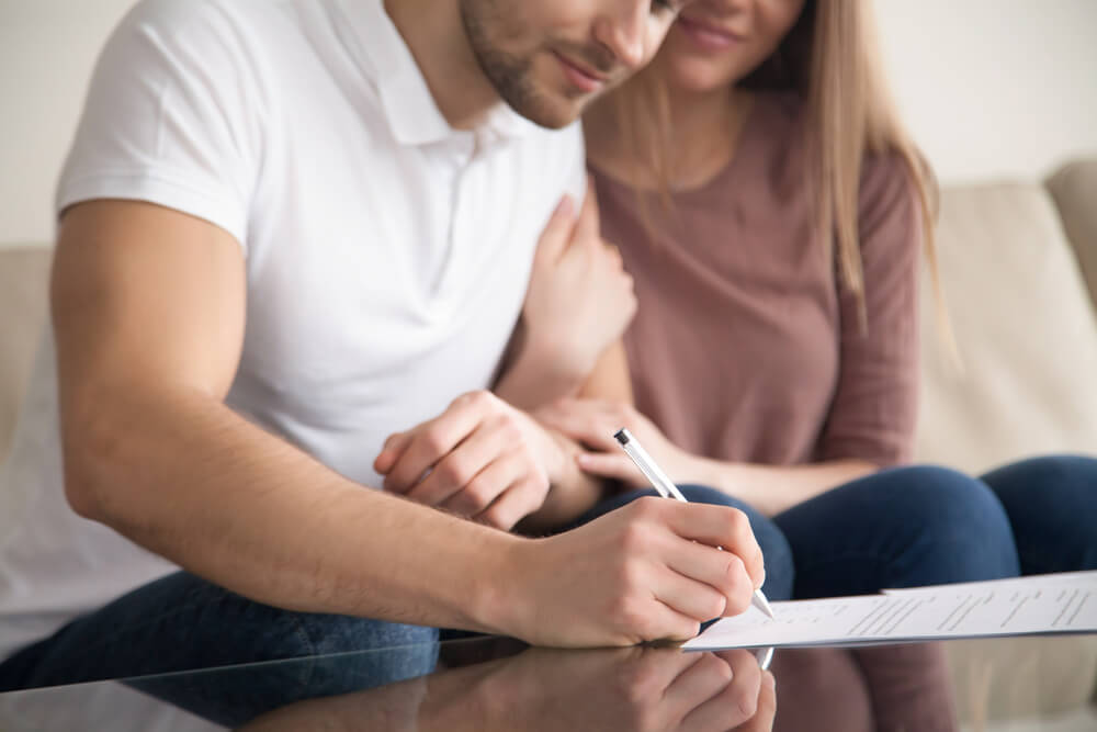 Man signing a prenuptial agreements with fiance holding his arm